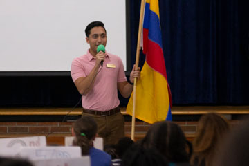 Man holding flag of Colombia in front of student assembly