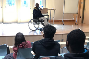 Man in wheelchair on stage speaking to students