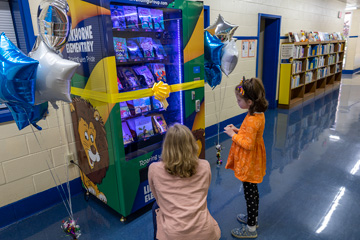 Student with librarian looking at book vending machine that is wrapped with Linkhorne Elementary graphics