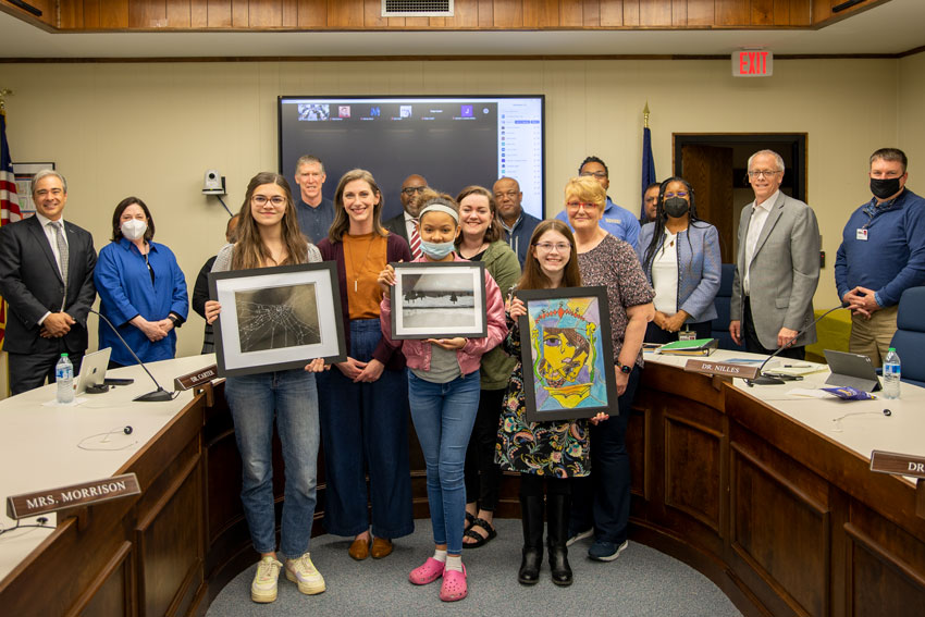 Students holding artwork standing with teachers and School Board members