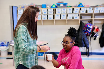 Teacher placing "money" in a cup a student is holding