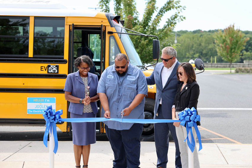 Transportation staff member with LCS administrators cutting ribbon in front of EV bus