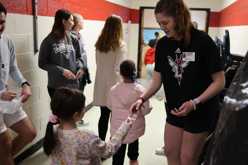 College athletes handing stickers to elementary students