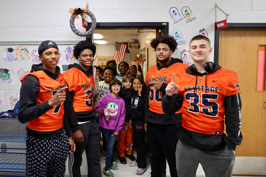 High school football players standing outside elementary classroom full of students