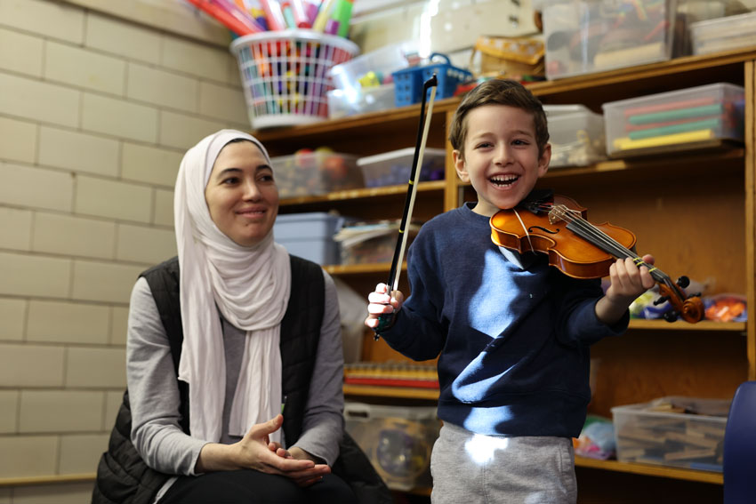 Student smiling holding violin with parent in background