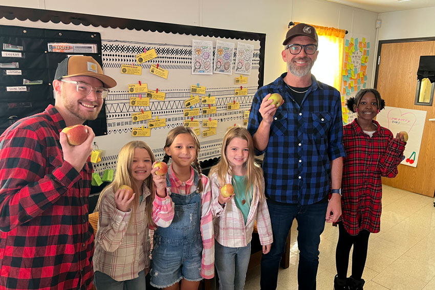 Two adults and 4 students in classroom holding apples