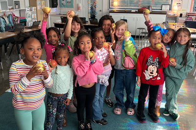 Group of students in classroom smiling and holding apples