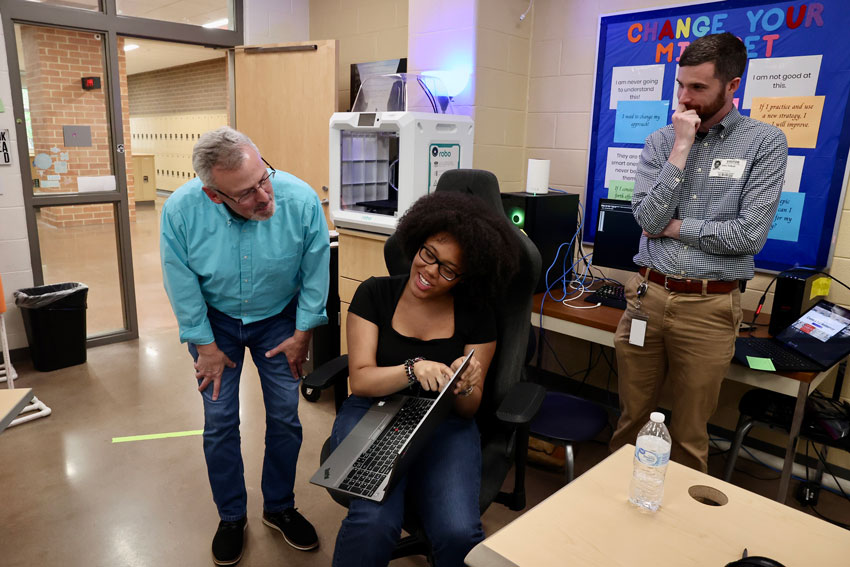 Teacher and community partner working with student in cybersecurity classroom