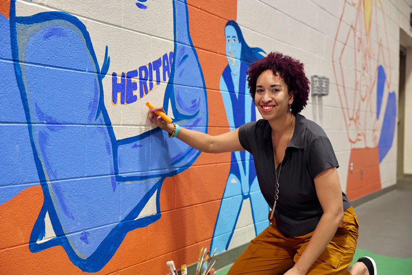 Artist, Christina Davis, working on mural in high school gym