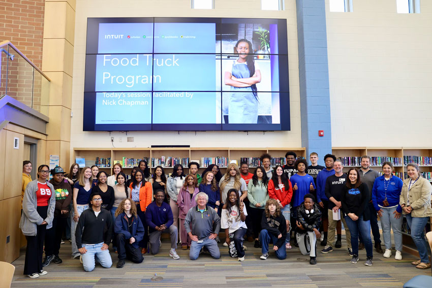 Group of students and adults in library with "Food Truck Program" presentation visible in background