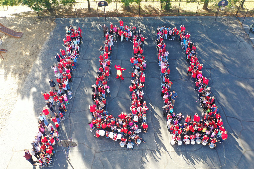 Aerial photo of students and staff arranged to spell "100"