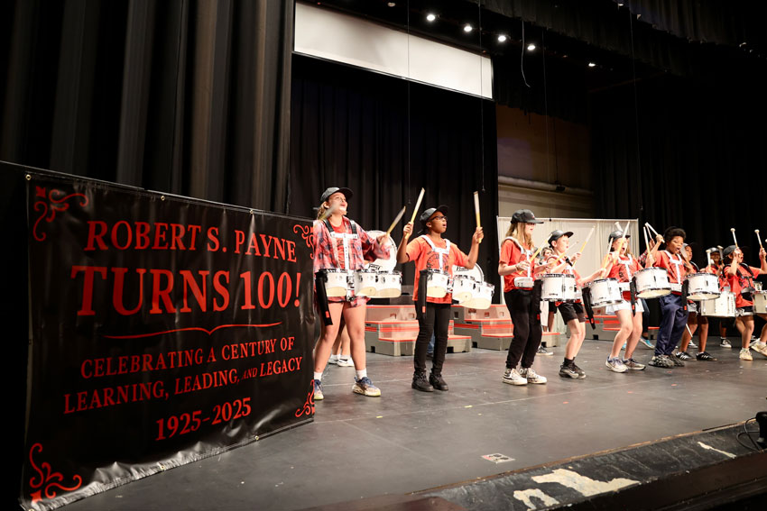Elementary drum line performing next to banner reading "Robert S. Payne Turns 100!"