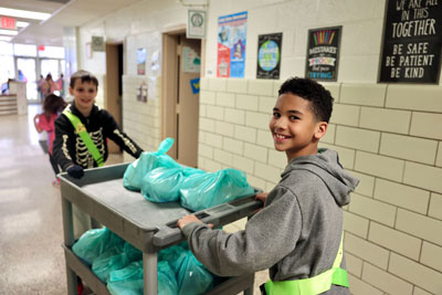 Two students wearing safety patrol belts rolling a cart in hallway