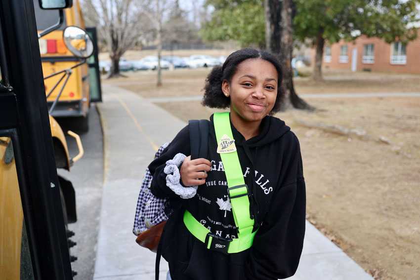 Student in safety patrol belt next to school bus