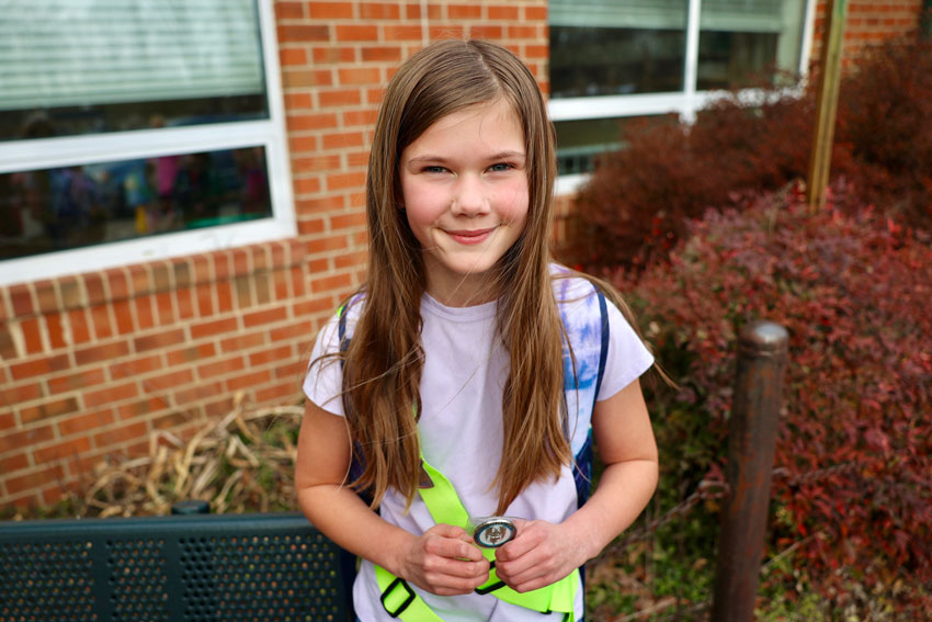 Student in safety patrol belt holding challenge coin