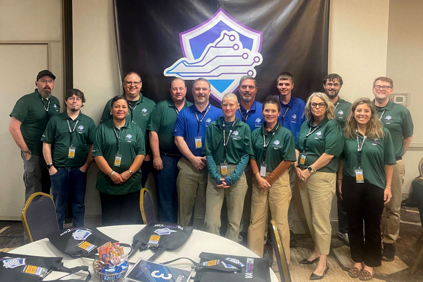 Group of IT staff standing in front of Virginia Cybercon banner