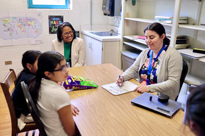 Teacher working with students in small group with Superintendent watching in background