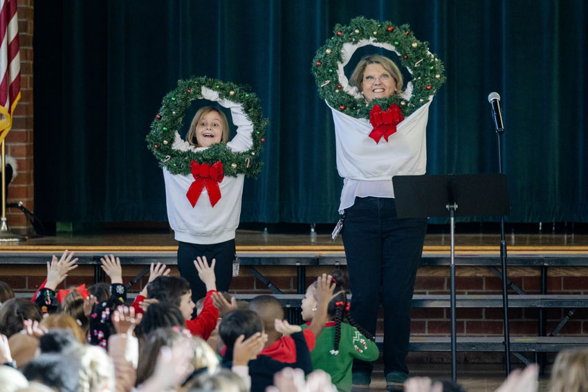 Elementary student and principal in matching sweatshirts leading crowd during school assembly