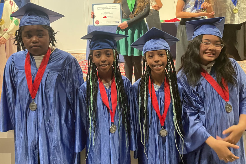 Four elementary students in caps and gowns wearing competition medals