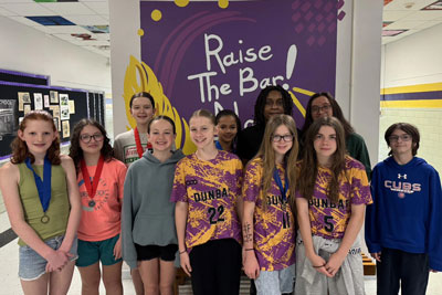 Eleven middle school students standing in front of Dunbar Middle School mural, some wearing competition medals