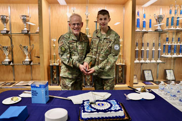 JROTC instructor and student cut cake with sword in front of school trophy case