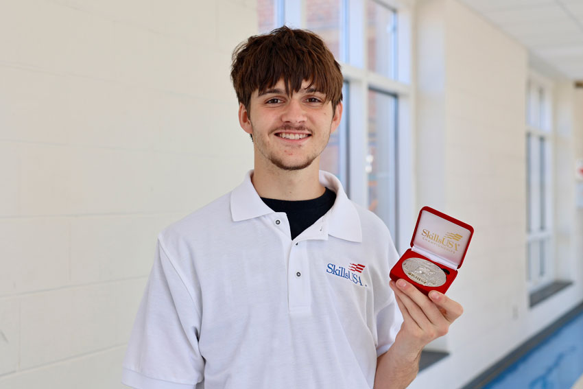 Student, Ezra Mancier, holding SkillsUSA award in school hallway
