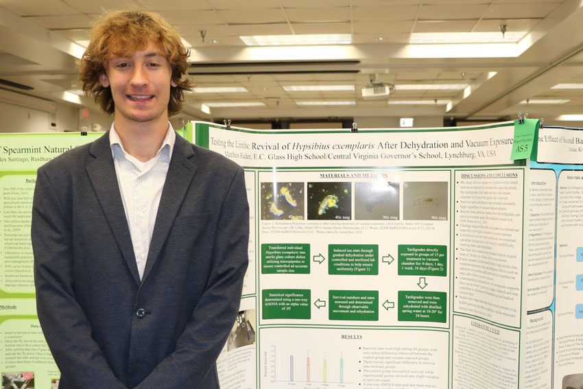 High school student in professional attire standing in front of science fair display with title “Testing the Limits: Revival of Hypsibius exemplaris After Dehydration and Vacuum Exposure.”