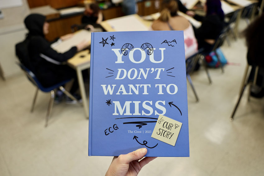 Hand holding yearbook with "You Don't Want to Miss Our Story - ECG" on the cover