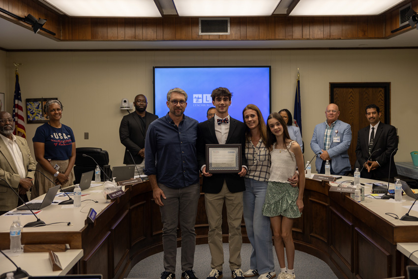 Scholarship recipient holding certificate in front of School Board members in Board Room