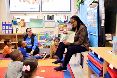 Superintendent reading to students seated on colorful rug in a classroom