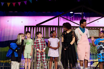 High school drama students in costume interacting with elementary student with set pieces in the background