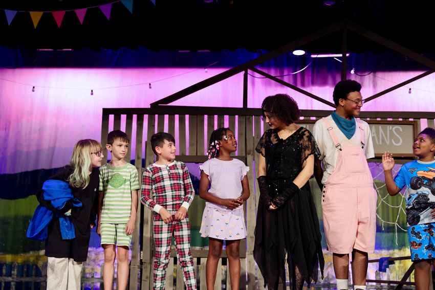 High school drama students in costume interacting with elementary student with set pieces in the background