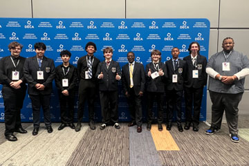 Group of students in business attire with their teacher in front of DECA backdrop