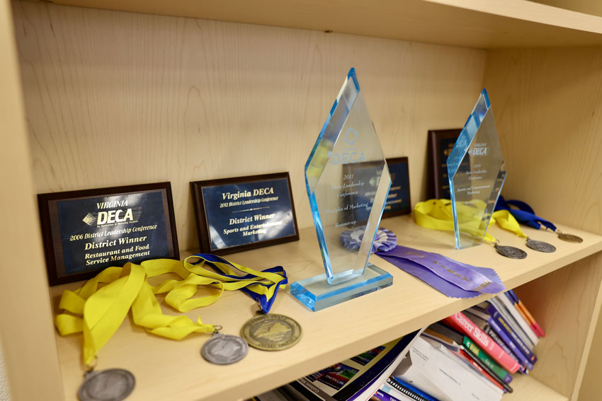 DECA medals, recognition plaques and trophies on bookshelf.