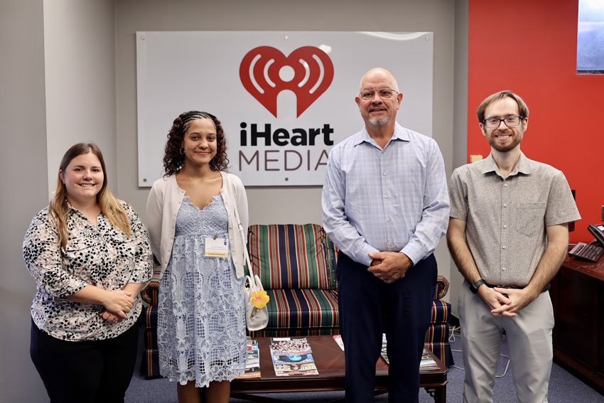 Student with community partners standing front of iHeart Media sign