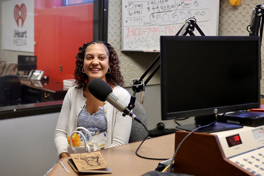 Student smiling while seated in front of microphone in radio studio