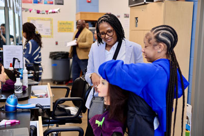 Superintendent watching cosmetology student styling hair of mannequin head