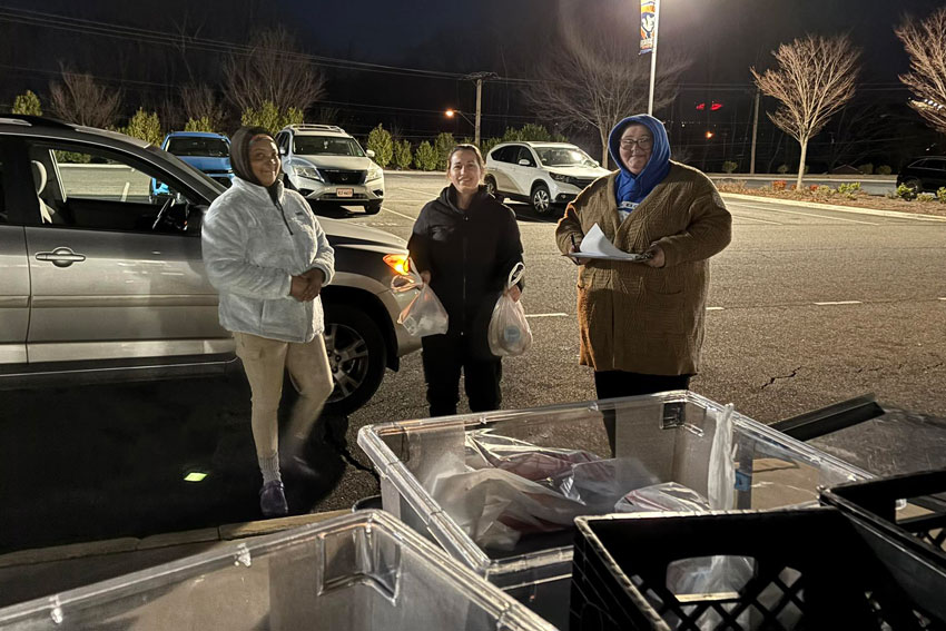 Three adults in parking lot, one holding bags of food