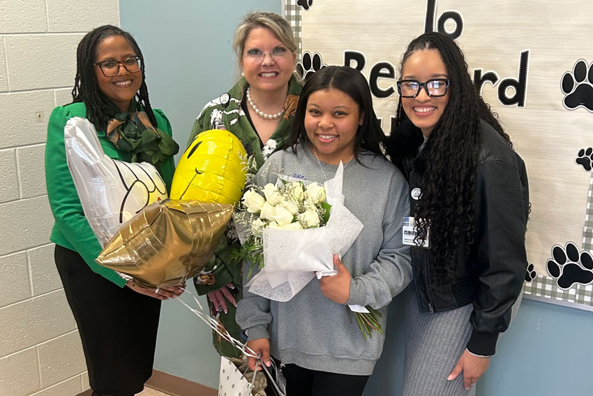 Mia Reeves holding balloons and flowers surrounded by superintendent, principal and assistant principal
