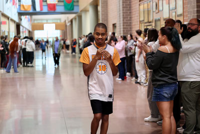 Basketball player in hallway with staff and students clapping in background