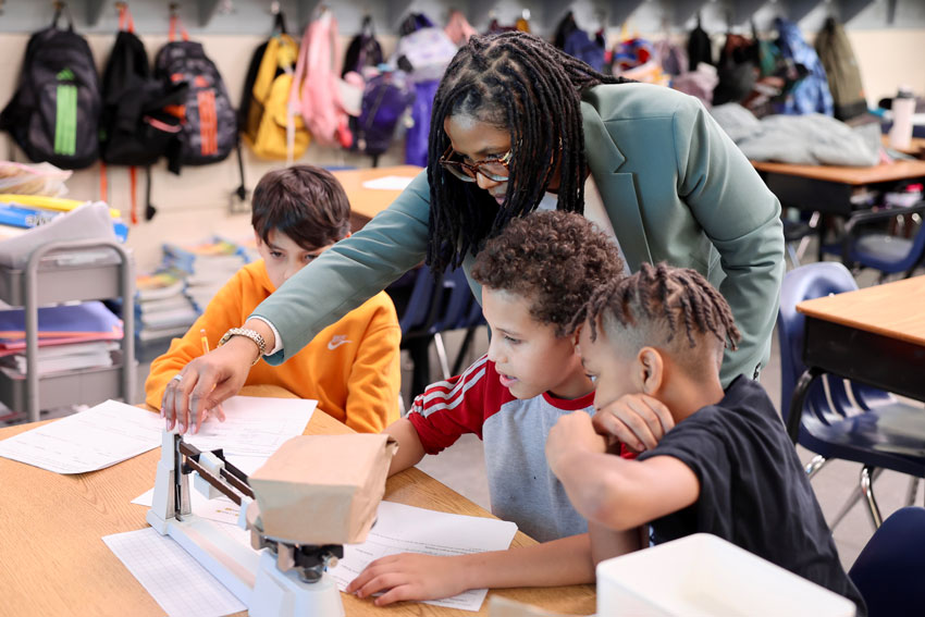 Superintendent with three boys using scale to complete classroom project