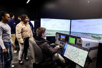 Middle school student at controls of flight simulator while two classmates watch from the side