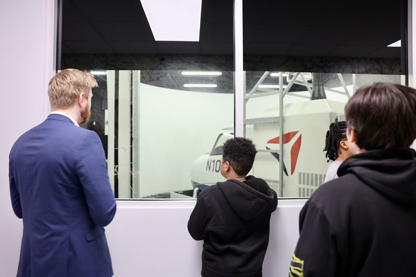 Middle school students with college representative looking through glass at aviation equipment