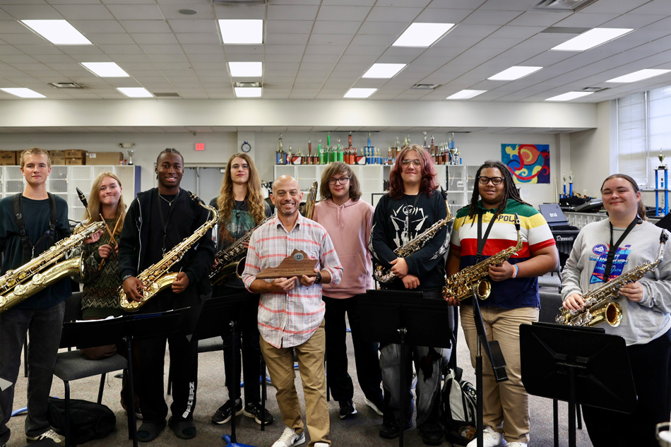 Band director holding VBODA award with students holding instruments behind them