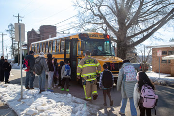 Line of students with firefighter in front of school bus in snowy conditions