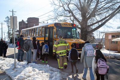 Line of students with firefighter in front of school bus in snowy conditions