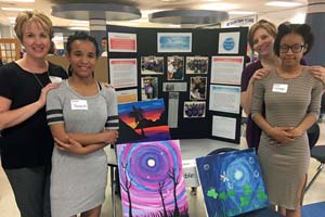 Two students with teachers standing with paintings