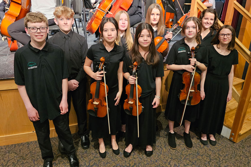 group of 9 orchestra students standing in front of a stage