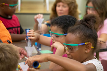 Two girls wearing goggles pouring liquid in tube