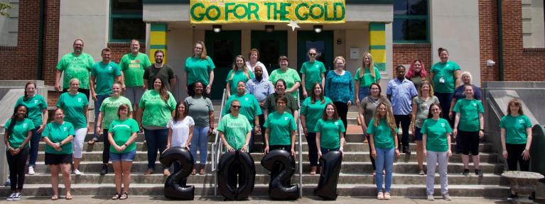 Bass staff standing on steps with Go for the Gold banner in background